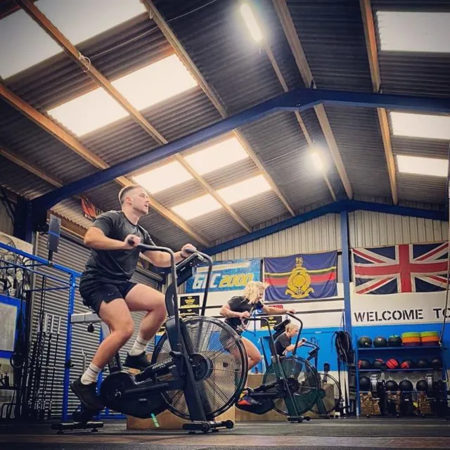 A member on the air bike in front of the Royal Marines flag and the Union Jack