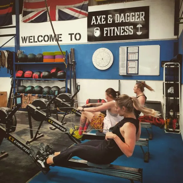 Members racing on the rowing machines below the Welcome to Axe & Dagger Fitness sign