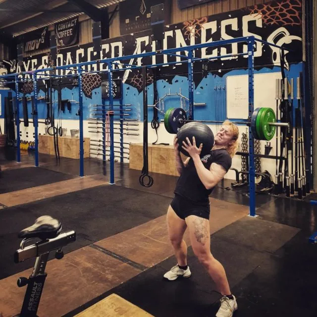 A member squatting with a wall ball in front of the Axe & Dagger Fitness wall